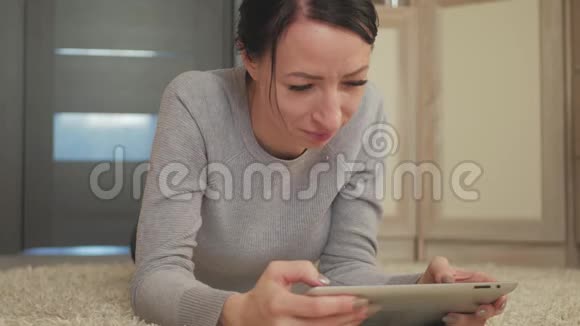 年轻体贴的黑发在家地毯上使用数字平板电脑在地板地毯上躺着的漂亮女人视频的预览图