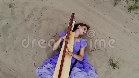 在沙漠里躺在沙滩上弹奏竖琴的女竖琴师的无人机射击视频的预览图