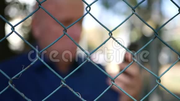 男子在金属围栏后面与手机通话的模糊射击视频的预览图
