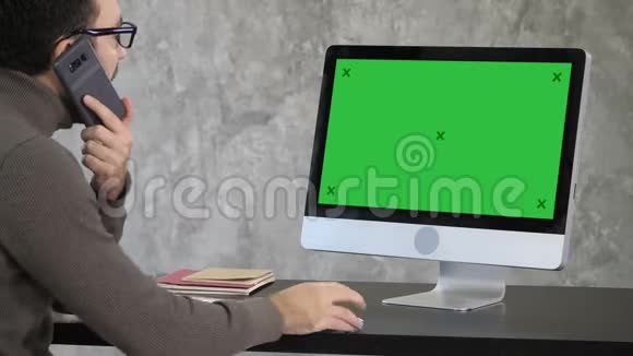 严重集中的男性上班族用手机打电话在电脑上工作绿色屏幕模拟显示视频的预览图