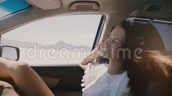 特写POV拍摄的快乐放松的女人与飞扬的头发眼睛紧闭在乘客座位上沿着盐湖沙漠移动视频的预览图