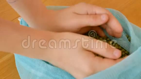 幼儿双手在木制背景上用蓝色可重复使用的包装玩绿色绿豆葡萄生态包装视频的预览图