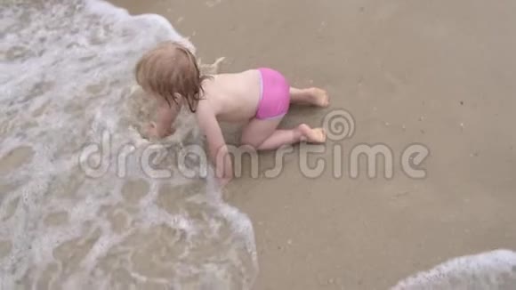 婴儿在波浪中在水面上爬行小女孩在沙滩上潮湿的沙滩上爬行视频的预览图