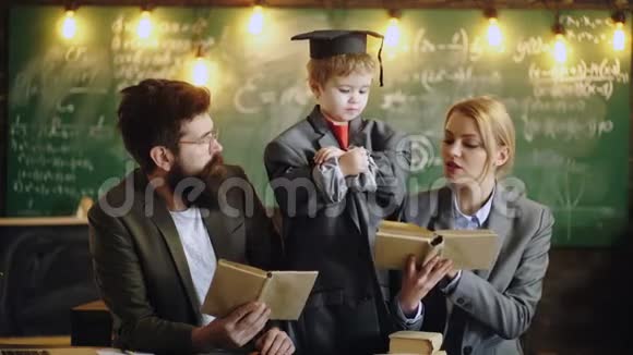 孩子在学校教女人和男人带大西装外套和毕业帽的孩子和家人一起在办公桌前考试视频的预览图