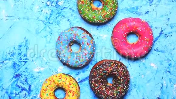 五颜六色的美味甜甜甜圈在蓝色的背景上旋转慢动作视频特写视频的预览图
