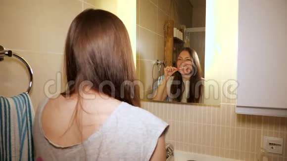 年轻的女人早上在浴室里刷牙看着镜子视频的预览图