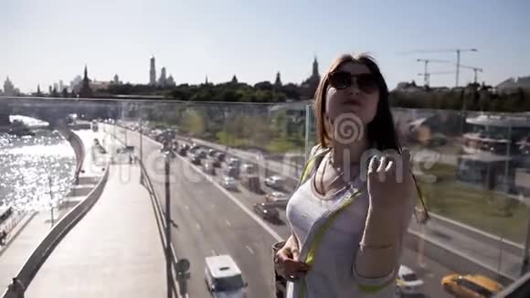 美丽的女孩戴着太阳镜长发在桥上日落时使用智能手机应用程序视频的预览图