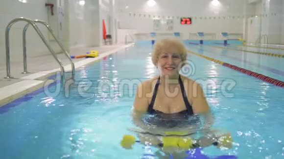 漂亮的老年妇女在游泳池里用哑铃做运动视频的预览图
