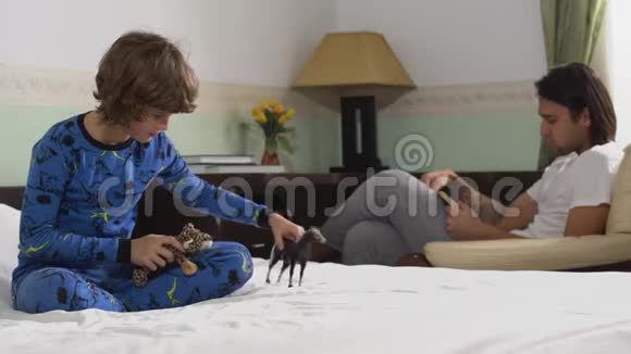 一个孩子在床上玩马虎玩具哥哥在扶手椅上看书兄弟会视频的预览图