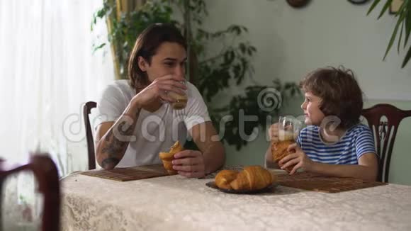 两个兄弟坐在厨房的桌子上吃着牛角面包和卡布奇诺哥哥和弟弟们在聊天视频的预览图