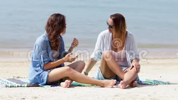阳光明媚的一天两个年轻的女人正在海滩上听音乐视频的预览图