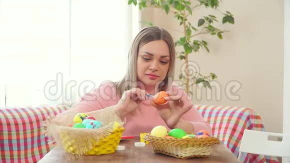 妈妈端着一篮子彩蛋坐在桌旁在一个鸡蛋上画一个蓝色的画笔他的女儿说视频的预览图