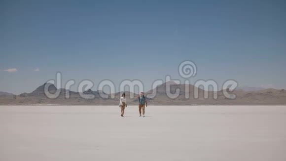 后景青年男子走向美丽的女人站在阳光明媚的热犹他盐漠湖的中间摆姿势视频的预览图