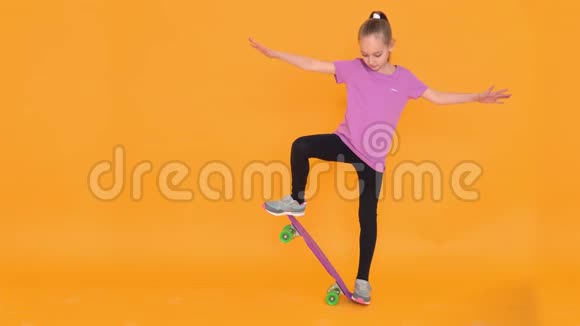 在橙色背景的工作室里少年女孩在滑板上保持平衡视频的预览图