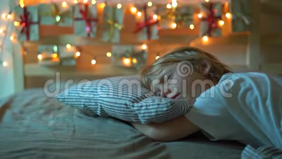 一个小男孩慢镜头醒来看到一张挂在床上的历法被圣诞灯光照亮视频的预览图