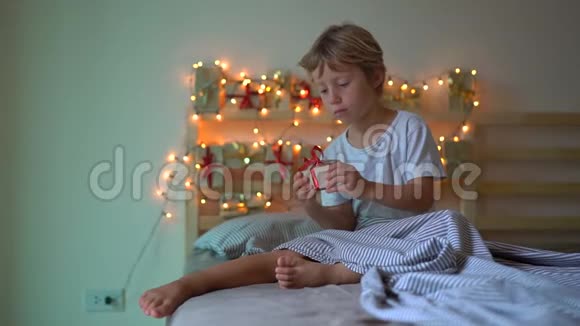 一个小男孩从一张挂在一张被点亮的床上的日历中打开礼物的慢镜头视频的预览图