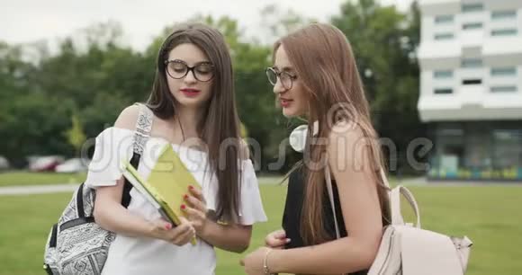 两个十几岁的女孩在校园里一起聊天两名女大学生在户外大城市建筑时视频的预览图
