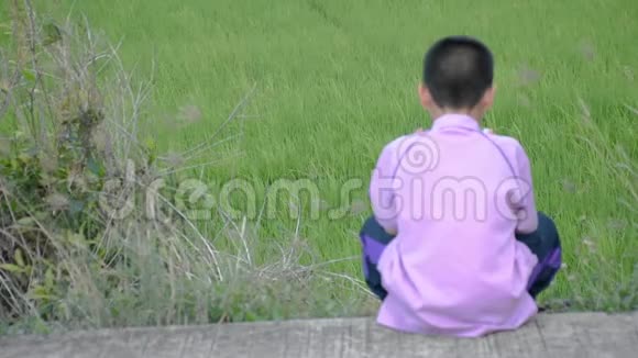 模糊的亚洲男孩拿着电话坐在街道上绿色的稻田视频的预览图
