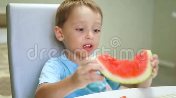 快乐的孩子坐在桌子旁高兴地在手里吃西瓜动作缓慢视频的预览图