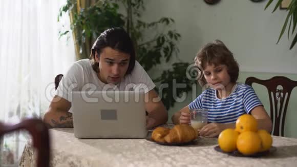 小男孩在厨房的桌子上吃东西喝卡布奇诺然后给他的成年兄弟橘子年长和年轻视频的预览图