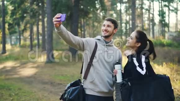 年轻人在公园里自拍手机摄像头摆着水瓶和运动袋视频的预览图