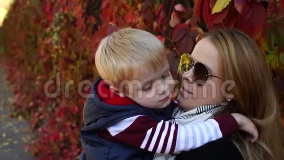 妈妈戴着太阳镜的特写在秋天公园拥抱她的小儿子视频的预览图