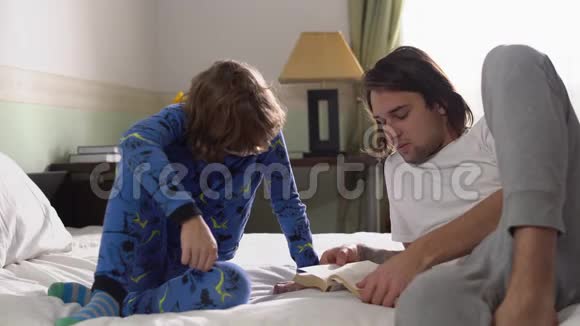 哥哥和弟弟穿着睡衣早上躺在卧室的床上兄弟读一本书给五个视频的预览图