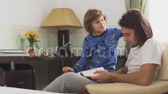 两个哥哥坐在扶手椅上哥哥给弟弟读了一本书小男孩摸着哥哥的长发视频的预览图