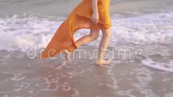 日落时女性光着脚和飘舞的裙子年轻的赤脚女孩穿着长裙子沿着冲浪线跑视频的预览图