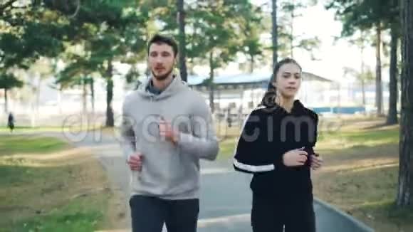 大胡子的年轻人和他的女朋友在公园里慢跑在户外运动穿着集中的现代运动服视频的预览图