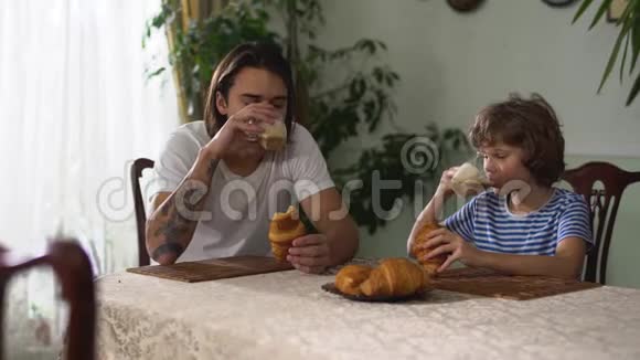 两个兄弟坐在厨房的桌子上吃着牛角面包和卡布奇诺哥哥抚摸着她的头视频的预览图