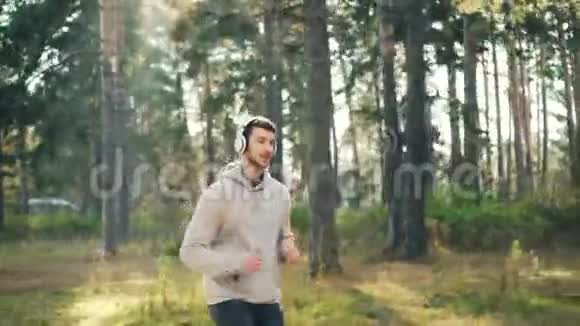 在公园里慢跑和听音乐的帅哥多莉镜头通过耳机欣赏歌曲和身体视频的预览图
