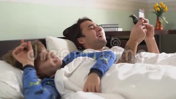 两个兄弟躺在铺着毯子的床上大个子在手机上聊天笑了起来兄弟关系视频的预览图