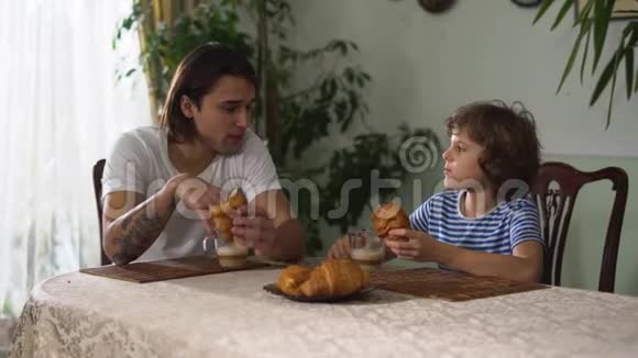 两个兄弟坐在厨房的桌子上聊天吃牛角面包喝卡布奇诺哥哥和弟弟视频的预览图