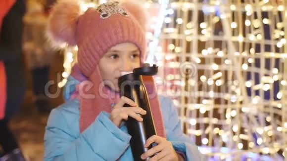 在市中心的圣诞晚会上小女孩喝着热水瓶里的茶视频的预览图