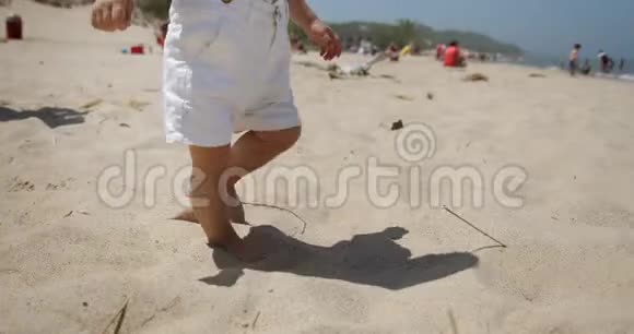 在沙滩上行走的不可辨认的小婴儿的腿慢动作特写视频的预览图