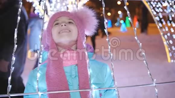 一个小女孩在市中心的圣诞集市上被花环和彩灯包围着玩视频的预览图