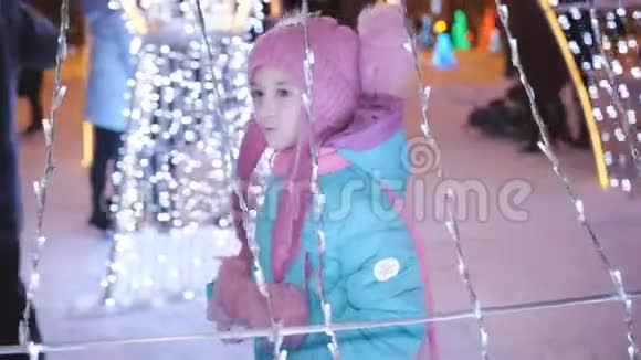 晚上在圣诞集市上的小女孩在彩灯和花环中度过了快乐而有趣的假期视频的预览图