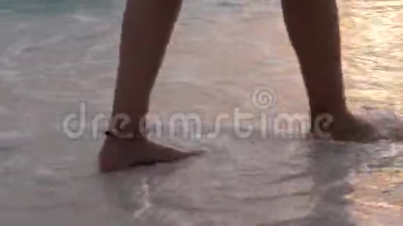 女腿沿着沙滩行走波浪在日落时冲走脚下的台阶光着脚的女孩视频的预览图