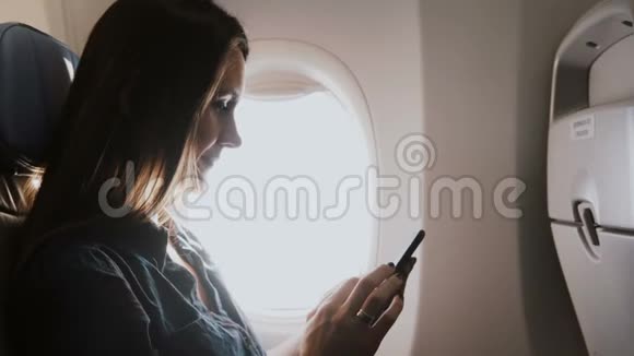 一位美丽快乐的欧洲年轻女商人在飞机靠窗的座位上使用智能手机购物应用程序的特写镜头视频的预览图