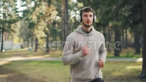 穿着时髦运动衫的帅哥正戴着耳机在公园里跑步夏天独自听收音机视频的预览图