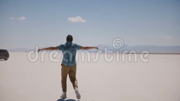 年轻快乐的男性游客张开双臂散步欣赏阳光明媚的盐漠湖史诗般的风景视频的预览图