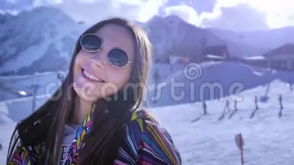 可爱的年轻女孩在冬天戴着太阳镜微笑在山上享受其余的冬季滑雪场玩得开心视频的预览图