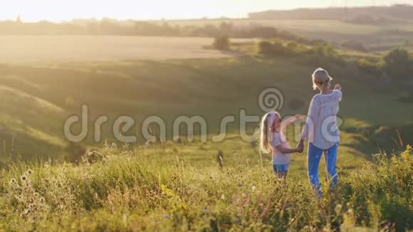 一个金发清凉的小女孩在绿色的田野上给妈妈看美丽的日落视频的预览图