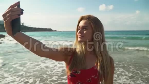 一幅可爱的年轻女子的肖像金发在海滩上的手机上自拍可爱的女孩花时间视频的预览图