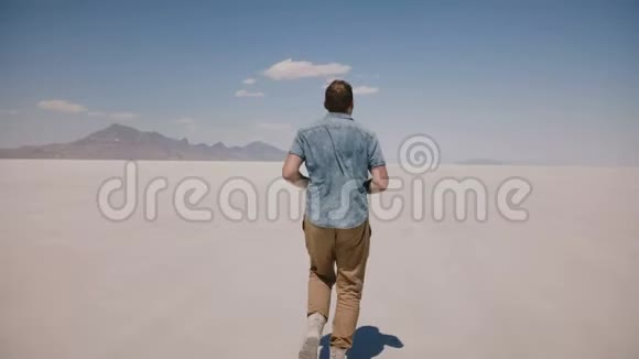 镜头跟随疲惫疲惫的年轻人在犹他州史诗般炎热阳光明媚的盐漠湖向蔚蓝的天空奔跑视频的预览图