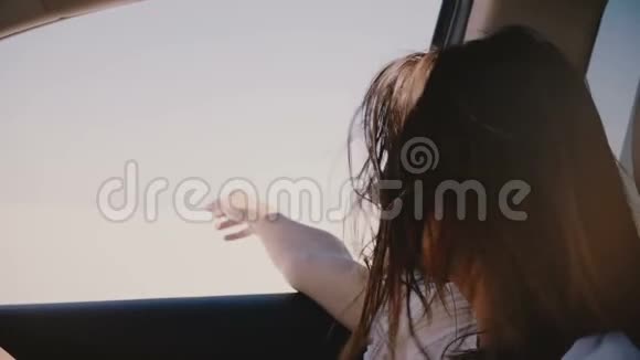 快乐的年轻旅游妇女头发飞扬手从窗外开着车沿着阳光明媚的盐湖沙漠前进视频的预览图