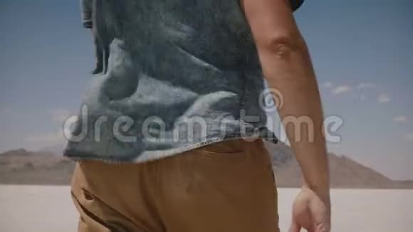 特写镜头跟随着穿着休闲服装的自由男人走着环顾美国犹他州多风的盐湖沙漠视频的预览图