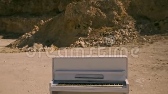 日落时白色的钢琴站在黄沙上映衬着岩石的背景超真实的情节视频的预览图