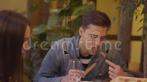 一对年轻夫妇用刀叉吃披萨在餐桌旁的现代意大利咖啡馆喝酒男人和女人有视频的预览图